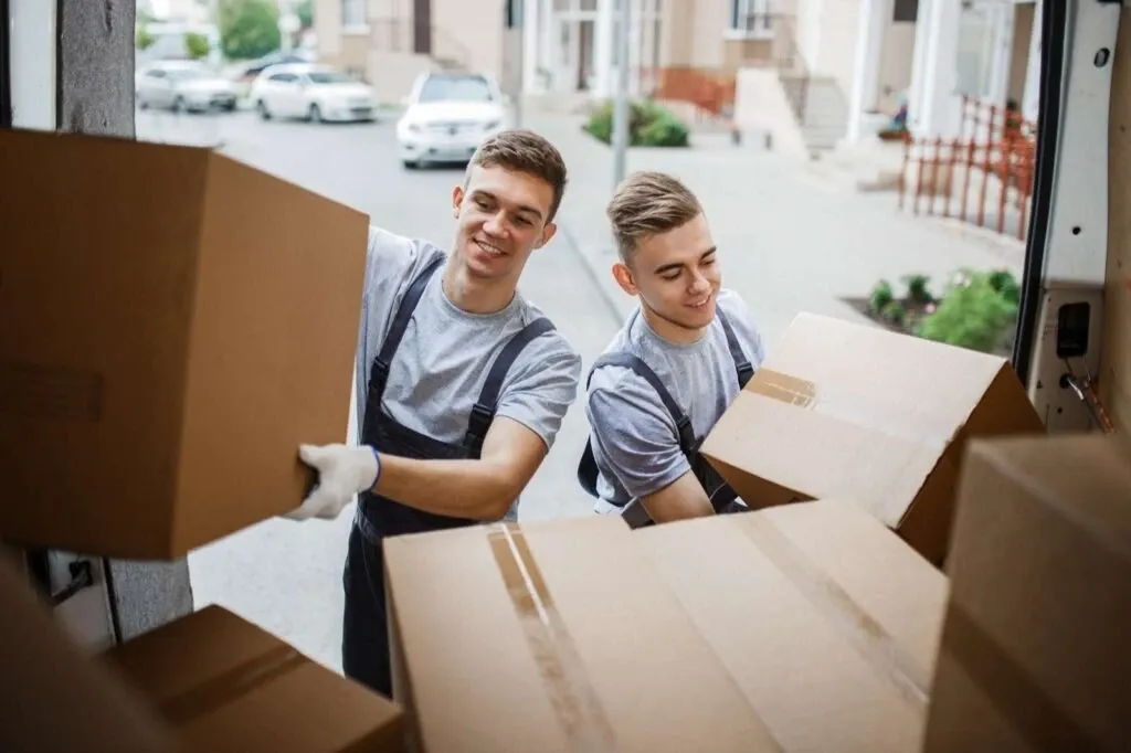 Two young handsome smiling movers loading boxes into moving truck